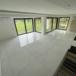 Welldonebathrooms.com - Jasne, marmurowe płytki podłogowe w przestronnym wnętrzu z dużymi oknami. Widoczne niedokończone schody i klimatyzator. Minimalistyczny design.