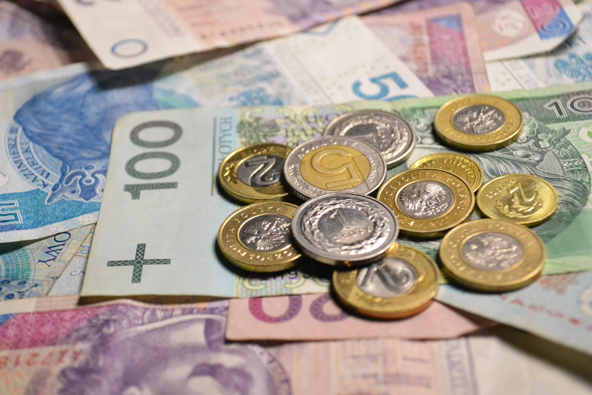 Stos banknotów (100, 50, 20 zł) i monet polskich (1, 2, 5 zł) w bliskim ujęciu. Symbol finansów, oszczędności, podatków i rozliczeń.