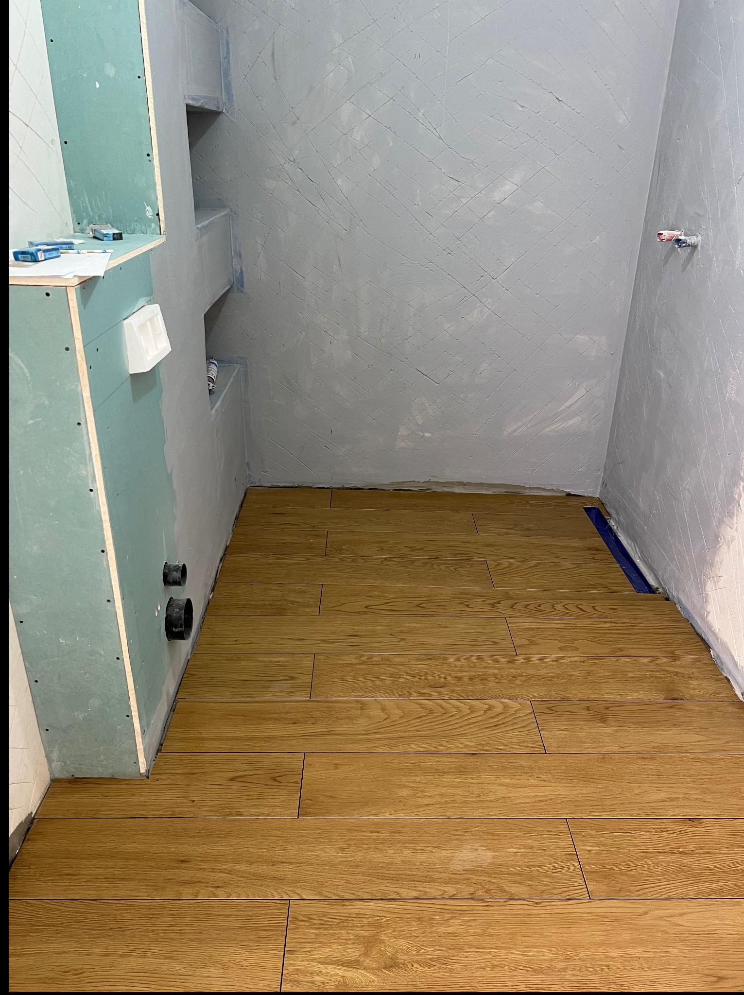 Układanie drewnopodobnej glazury w łazience w Myślenicach. Widoczne przygotowane ściany pod wykończenie i odpływ liniowy. Glazurnik Myślenice.