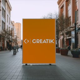 Creatik - Pomarańczowy billboard z białym logo 'CREATIK' na tle miejskiego deptaka z budynkami w stylu retro.
