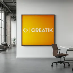 Nowoczesne biuro z plakatem w ramie z logotypem 'CREATIK' na żółtym tle, biurko z komputerem i krzesłem biurowym, industrialne okna w tle.