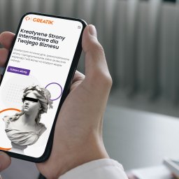 Creatik - Mężczyzna trzyma smartfon prezentujący stronę internetową z motywem klasycznej rzeźby, z tekstem o kreatywnych stronach internetowych dla biznesu i wezwaniem do działania 'Zobacz ofertę'.