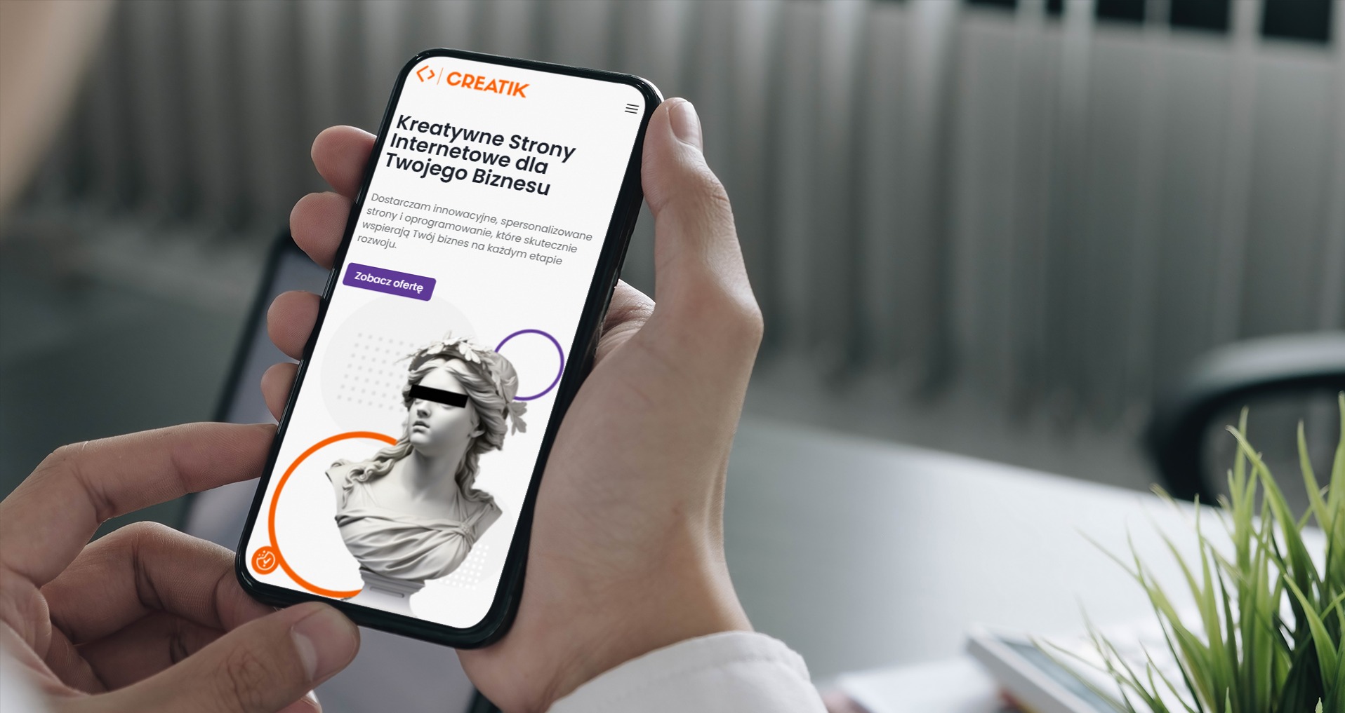 Mężczyzna trzyma smartfon prezentujący stronę internetową z motywem klasycznej rzeźby, z tekstem o kreatywnych stronach internetowych dla biznesu i wezwaniem do działania 'Zobacz ofertę'.