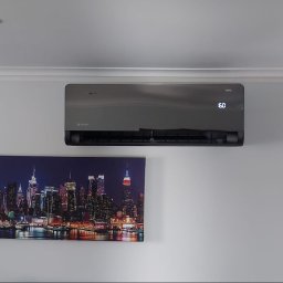 HEGEMON Sp. z o.o. - Szary klimatyzator ścienny z wyświetlaczem temperatury 16 stopni Celsjusza, zamontowany nad podświetlanym obrazem panoramy miasta nocą.