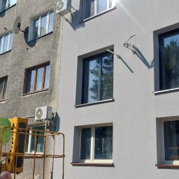 HEGEMON Sp. z o.o. - Montaż klimatyzatora na elewacji bloku w Gliwicach z użyciem podnośnika koszowego, widoczny pracownik w tle.