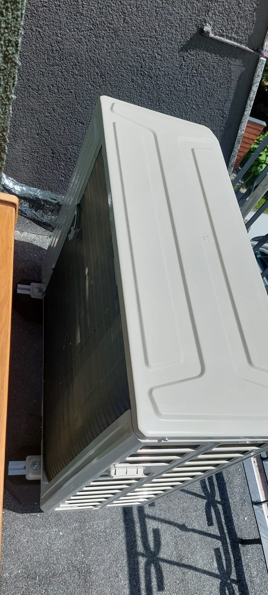 Zewnętrzna jednostka klimatyzatora zamontowana na elewacji budynku, widoczne żaluzje wentylacyjne i elementy mocujące.