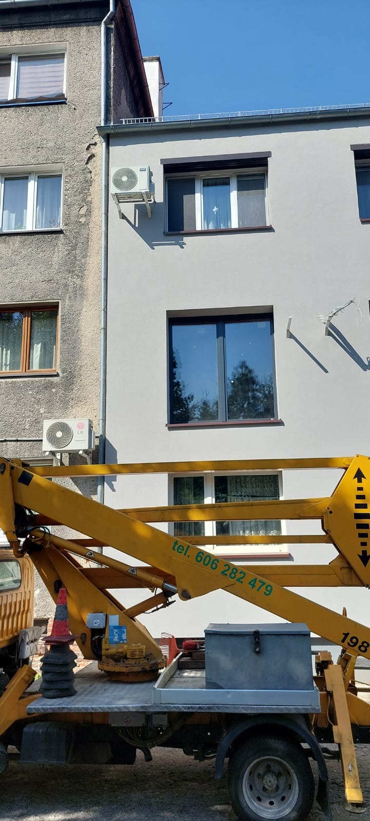 Montaż klimatyzacji LG na elewacji budynku, widoczny z podnośnika koszowego z numerem telefonu kontaktowym.