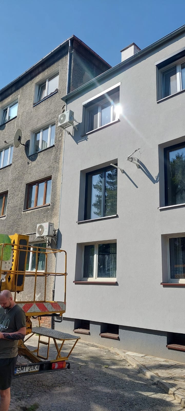 Montaż klimatyzatora na elewacji bloku w Gliwicach z użyciem podnośnika koszowego, widoczny pracownik w tle.