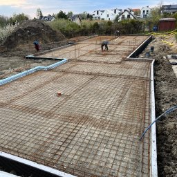 ArtM-Bud - Zbrojenie płyty fundamentowej z widoczną izolacją pionową i poziomą, pracownicy montują zbrojenie na budowie domu jednorodzinnego.