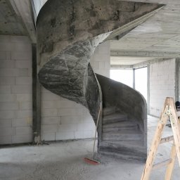 ArtM-Bud - Surowe betonowe schody spiralne w surowym stanie, wewnątrz budynku w trakcie budowy, widoczna drabina drewniana i miotła.