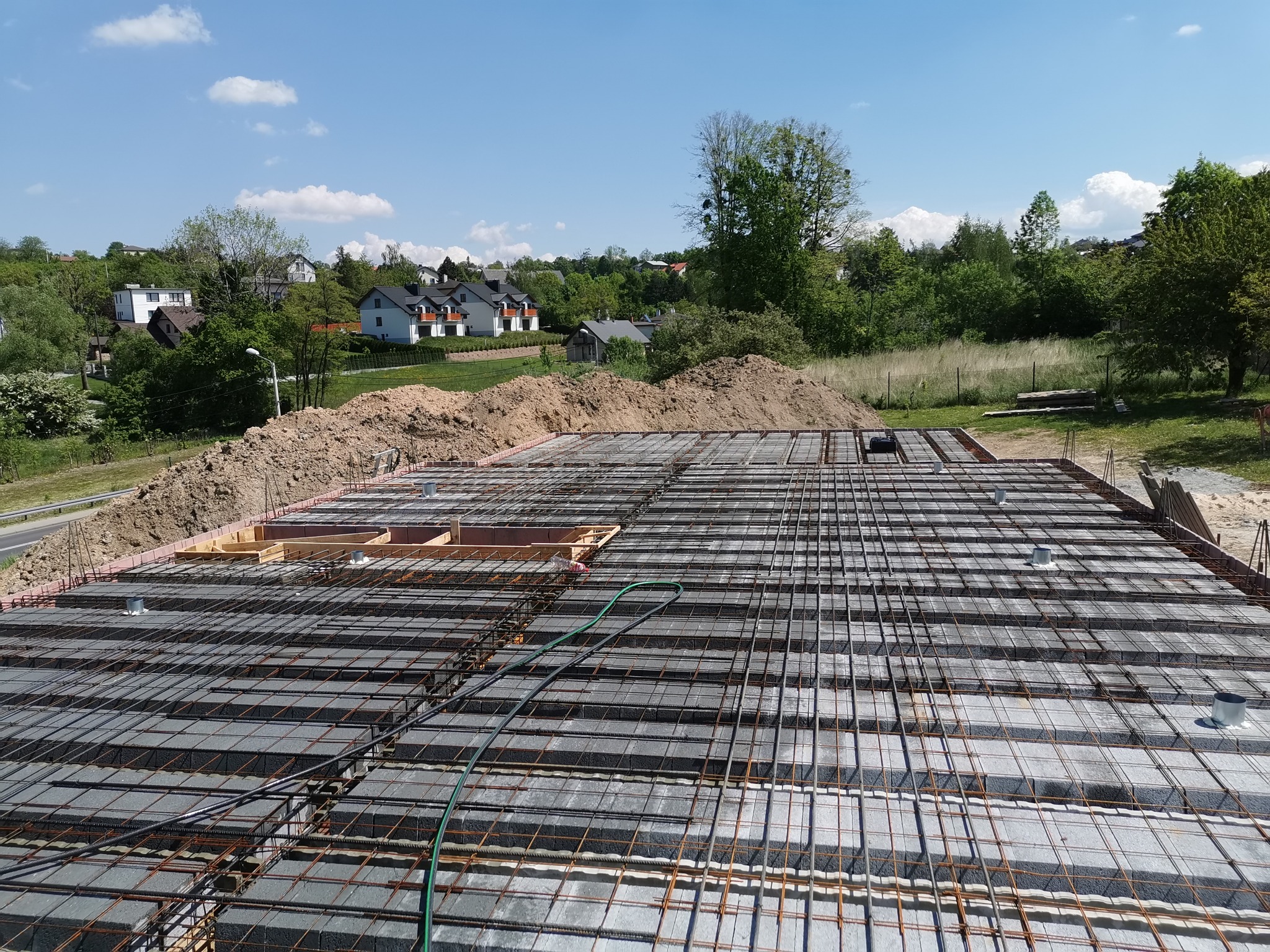 Zbrojenie stropu Teriva przygotowane do zalania betonem, widoczne szalunki obwodowe, w tle hałda ziemi i zabudowa jednorodzinna.