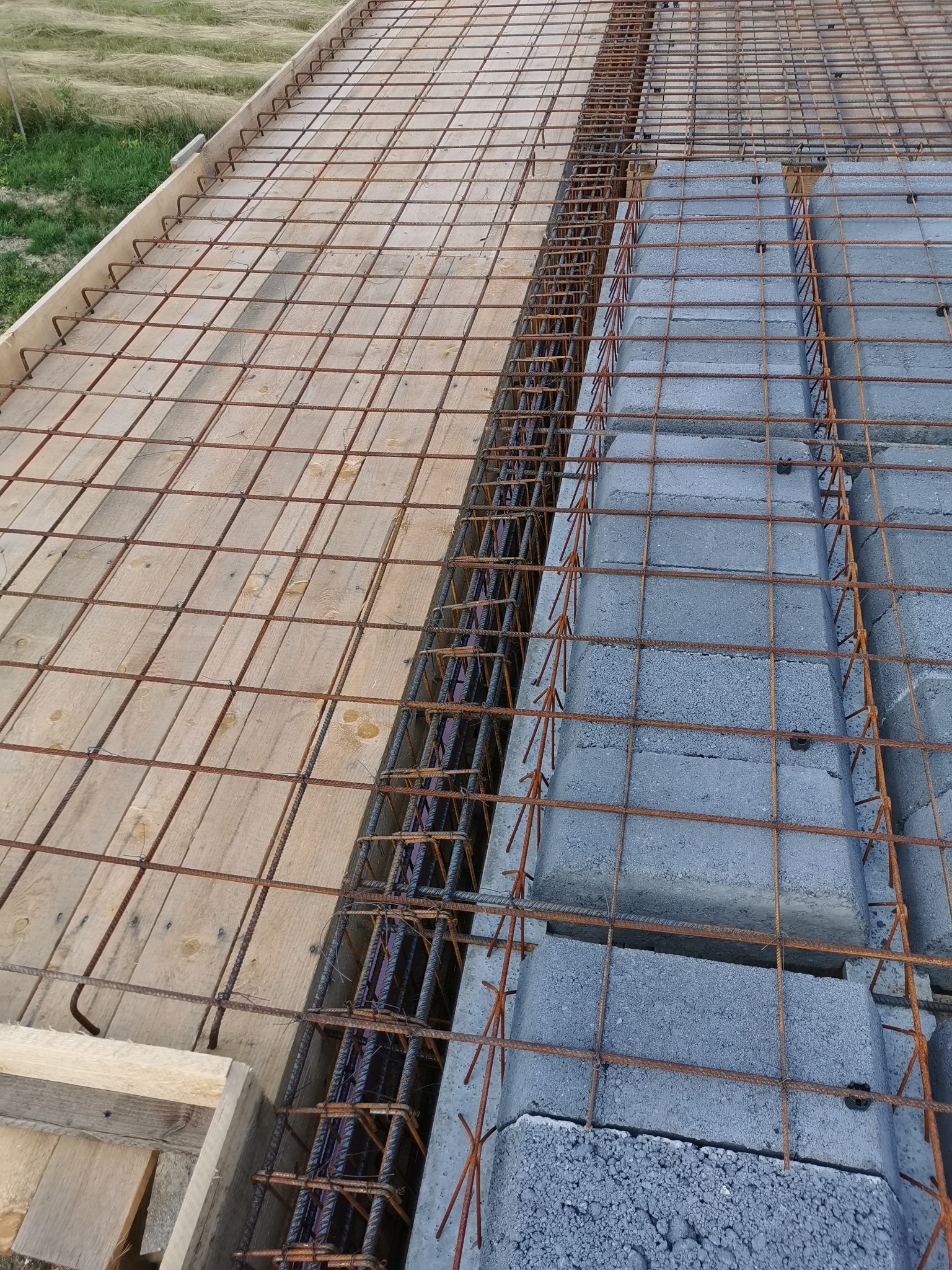 Przygotowanie szalunku i zbrojenia pod wylewkę stropu Teriva, widoczne bloczki betonowe i drewniane deskowanie, na zewnątrz teren zielony.