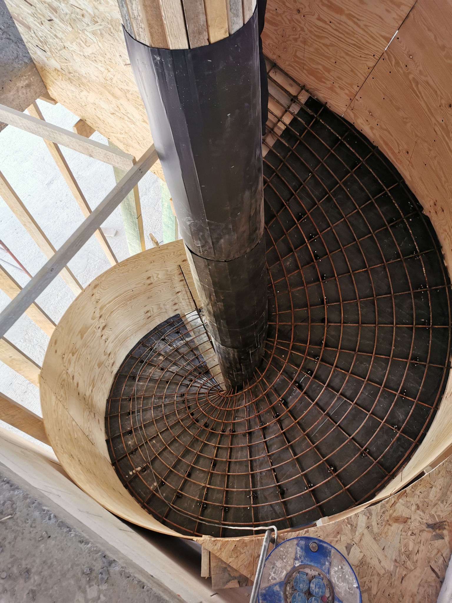 Wnętrze okrągłego szalunku z ułożonym zbrojeniem w formie siatki, przygotowane do zalania betonem, widok z góry.