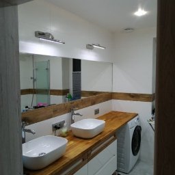 GK Remont - Nowoczesna łazienka w Wieliszewie z dwoma umywalkami na drewnianym blacie, dużym lustrem i pralką. Białe ściany z drewnianym akcentem. Oświetlenie punktowe.