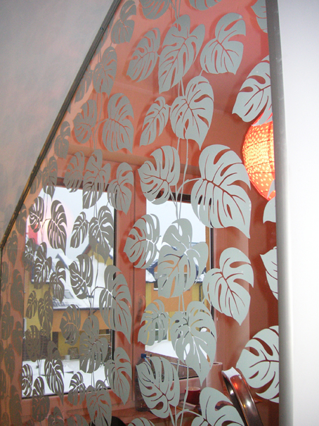 Folia dekoracyjna z motywem liści monstery na szklanej balustradzie schodowej, widok z dołu na okno i zimowy krajobraz.