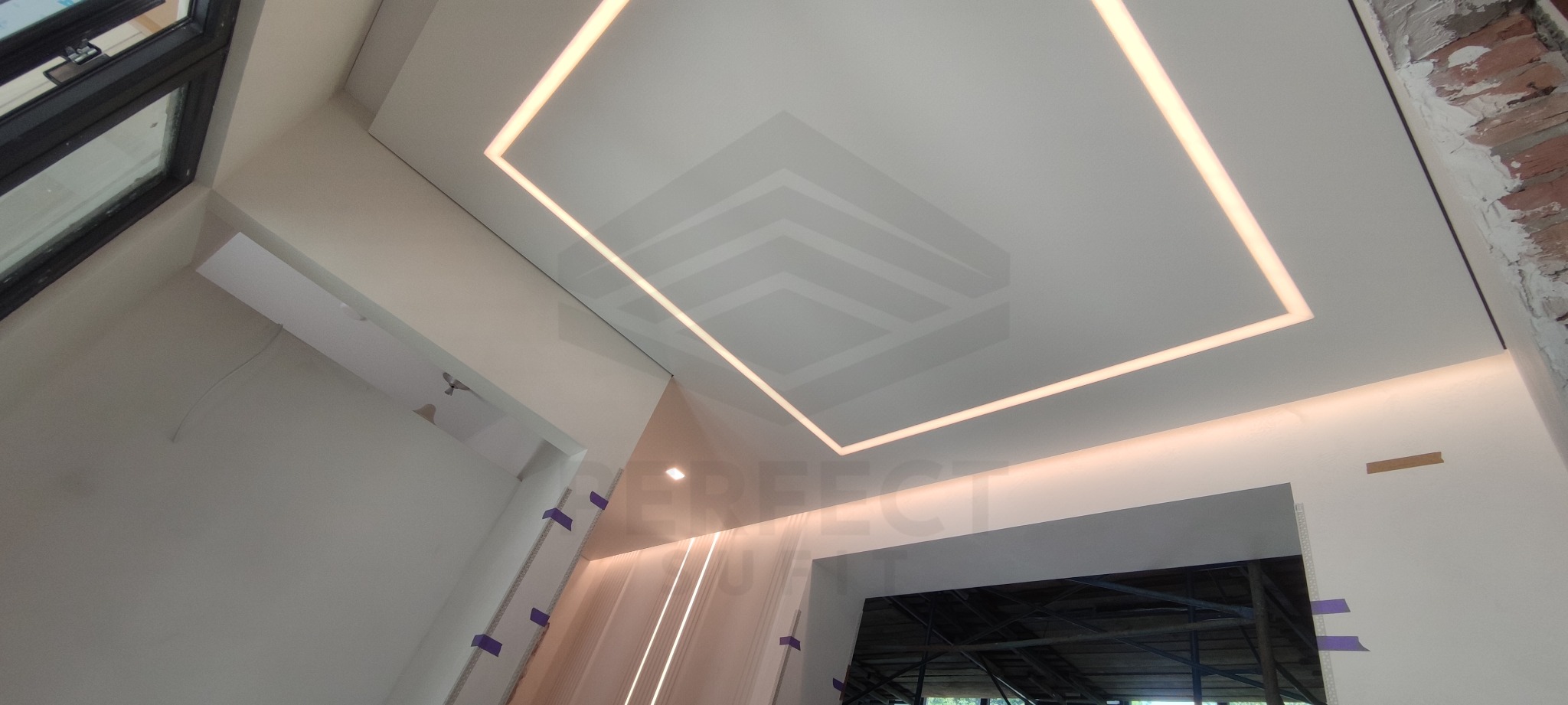 Biały sufit z wbudowanym oświetleniem LED w kształcie kwadratu, widok z dołu, fragment ściany z surową cegłą po prawej stronie.