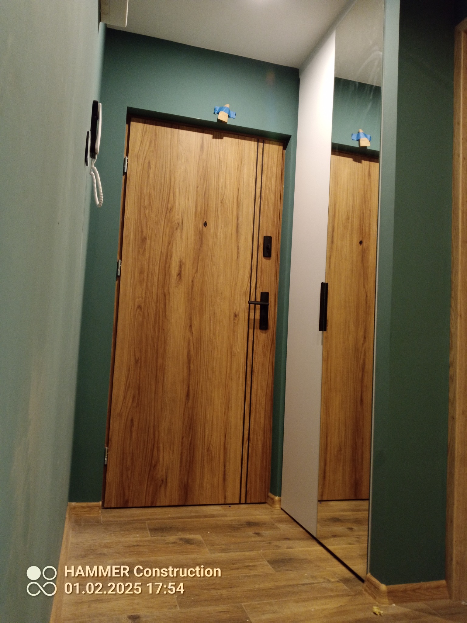 Montaż drzwi wewnętrznych z drewnianą okleiną w mieszkaniu w Motyczu, widoczne zabezpieczenia taśmą malarską.