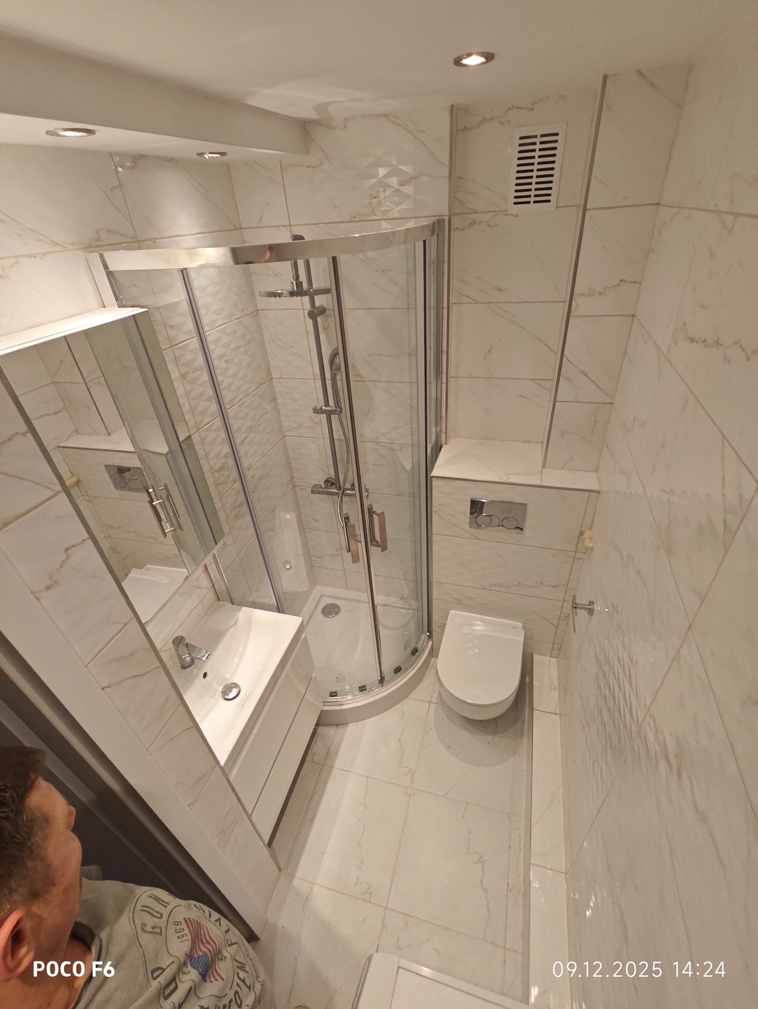 Wykończona łazienka w Szczecinie z kabiną prysznicową, umywalką i toaletą. Białe płytki imitujące marmur na ścianach i podłodze. Widok z góry.