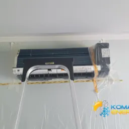 Klimatyzator ścienny marki DrA Best, zabezpieczony folią i taśmą malarską, z drabiny podczas montażu. Widoczne detale instalacji i logo firmy na ścianie.