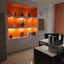 Nowoczesne biuro rachunkowe z pomarańczowymi wnękami na ścianie, w których ustawiono dekoracje, kwiaty i książki, biurka z komputerami i drukarką.