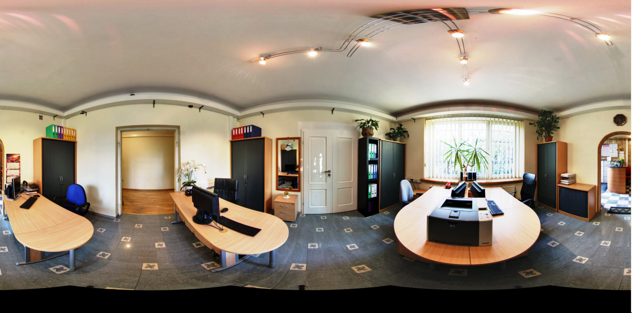 Panoramiczny widok przestronnego biura z trzema dużymi biurkami, szafami na dokumenty, roślinami doniczkowymi i oknem z żaluzjami.