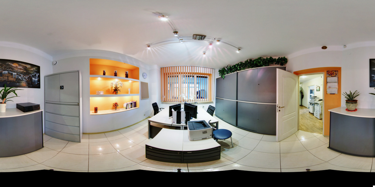 Panoramiczny widok wnętrza biura z biurkami, komputerami, szafami na dokumenty i elementami dekoracyjnymi w pomarańczowych wnękach.