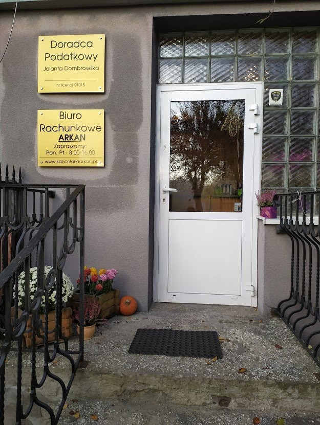 Wejście do biura rachunkowego i doradcy podatkowego z tabliczkami informacyjnymi, kwiatami w donicach i dynią dekoracyjną przed drzwiami.