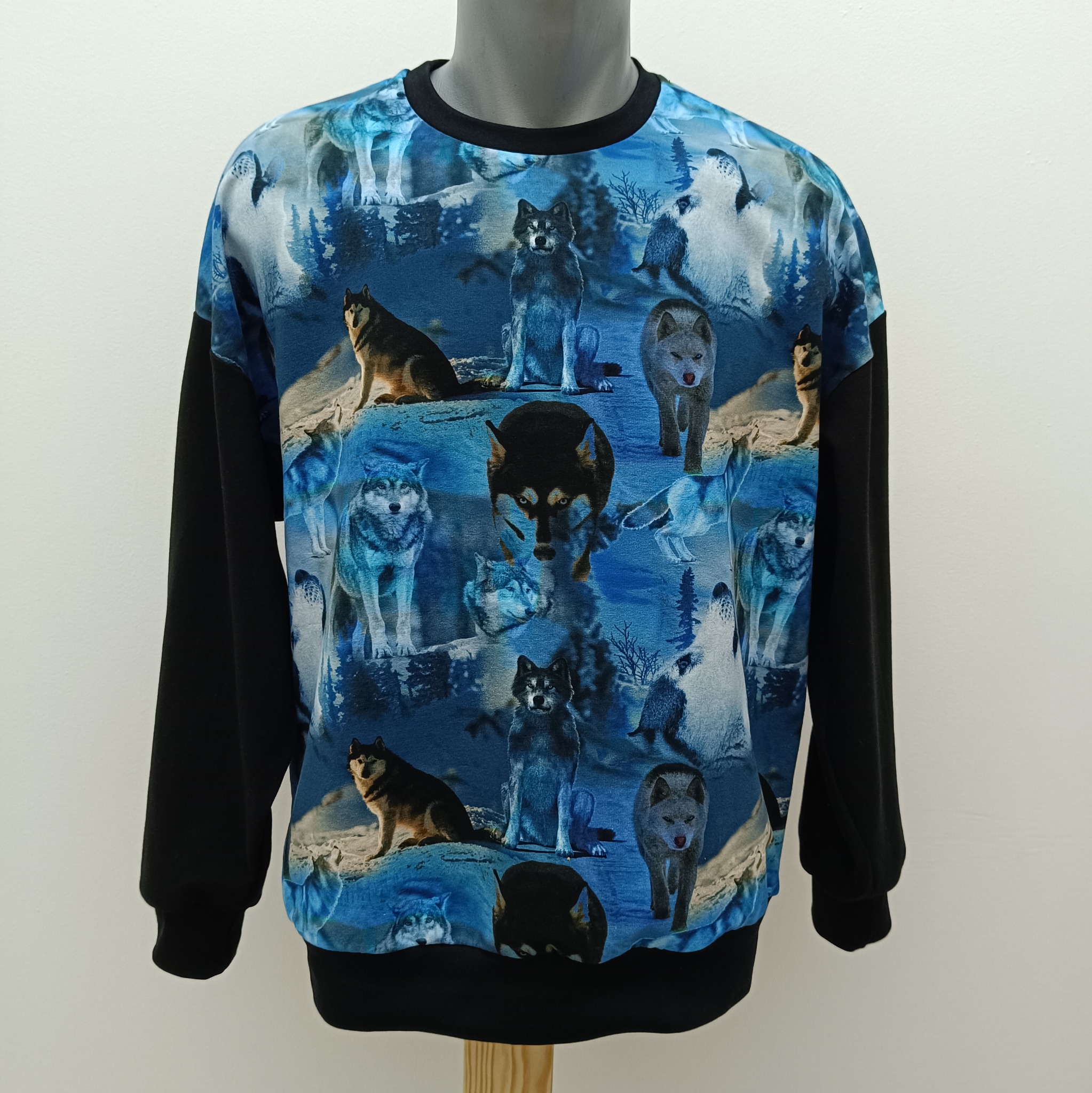 Bluza z długim, czarnym rękawem, z motywem wilków na niebieskim tle, zaprezentowana na manekinie na jasnym tle. Widoczne detale nadruku.