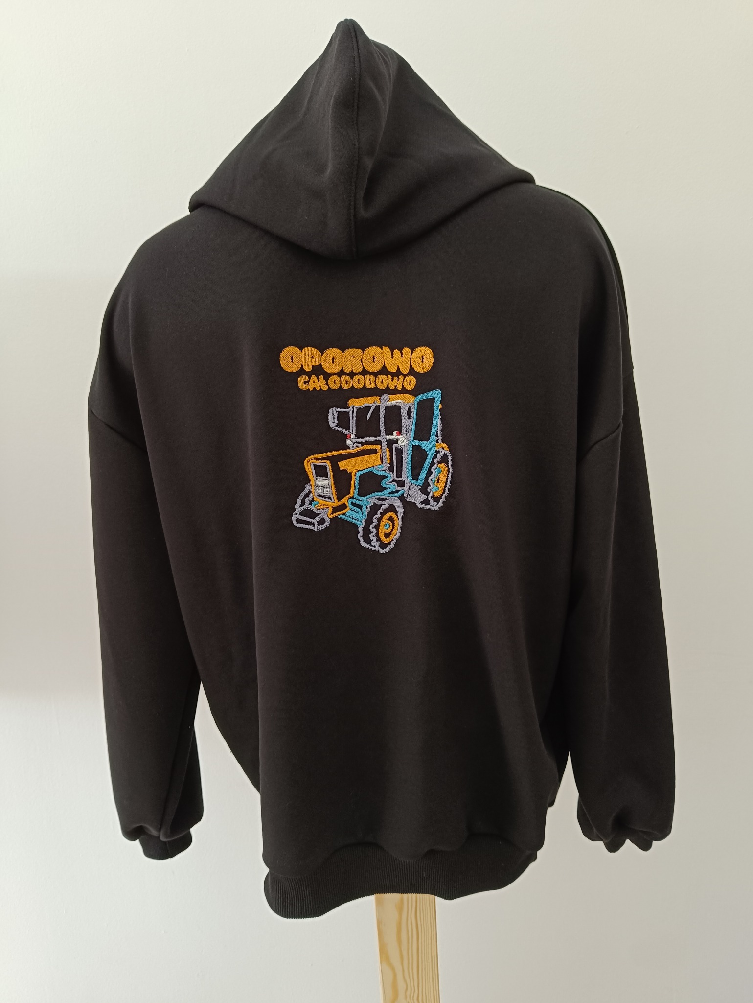 Czarna bluza z kapturem, na plecach haftowany kolorowy traktor i napis 'OPOROWO CAŁODOBOWO'.