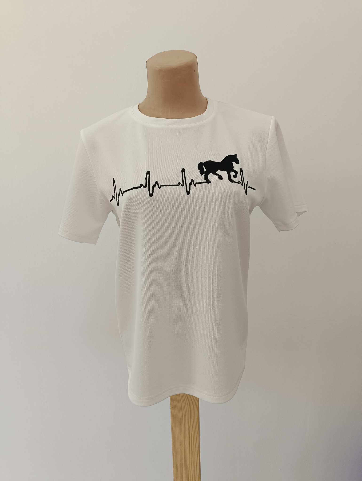 Biała koszulka polo z czarnym nadrukiem konia wkomponowanego w linię EKG, prezentowana na manekinie na tle białej ściany. Detal nadruku i materiału.