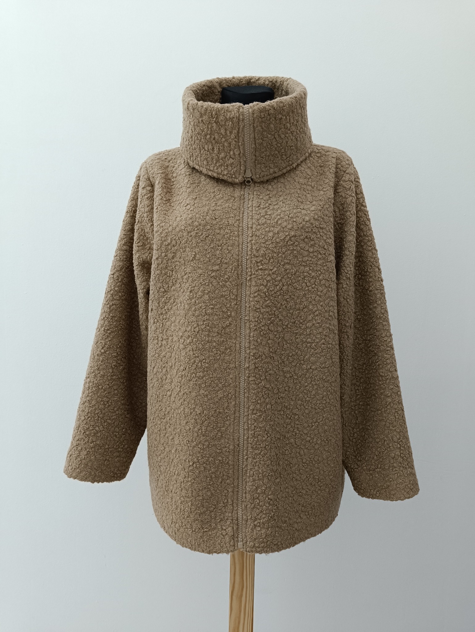 Beżowa kurtka damska z wysokim kołnierzem, zapinana na zamek, wykonana z pluszowego materiału typu baranek, prezentowana na manekinie na jasnym tle.