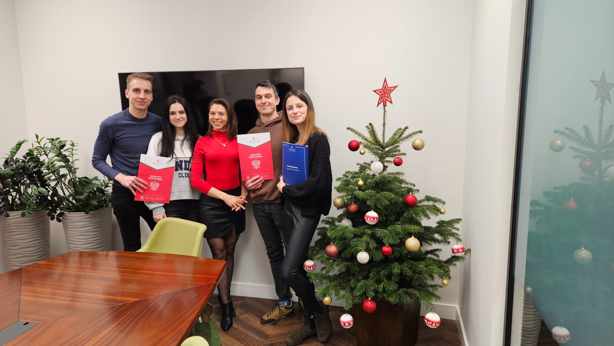Grupa pięciu osób trzymająca dokumenty w biurze z choinką, prawdopodobnie po podpisaniu umowy.