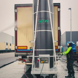 MTW Global - Automatyczna myjka do samochodów ciężarowych w trakcie pracy, operator w odzieży roboczej kontroluje proces, widoczny spływający strumień wody po karoserii pojazdu.