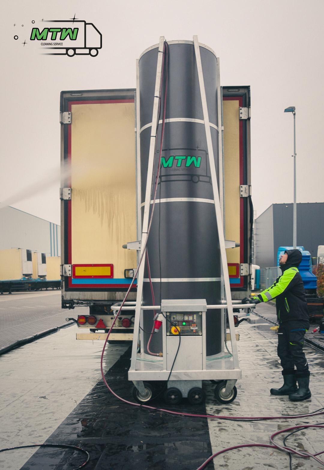 Automatyczna myjka do samochodów ciężarowych w trakcie pracy, operator w odzieży roboczej kontroluje proces, widoczny spływający strumień wody po karoserii pojazdu.