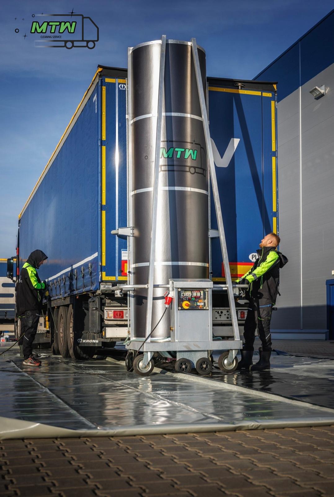 Dwaj pracownicy w odblaskowych kurtkach obsługują mobilną maszynę do czyszczenia burt niebieskiej naczepy ciężarówki z logo MTW na tle przemysłowego budynku.