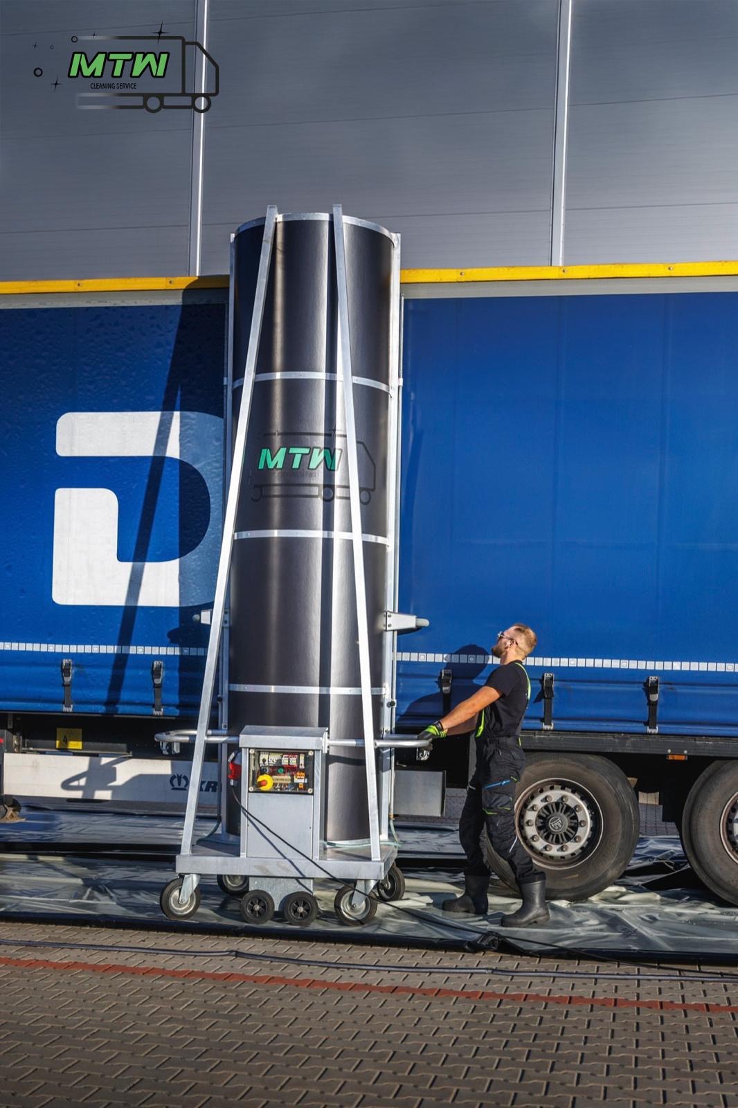 Pracownik obsługuje mobilne urządzenie do czyszczenia bocznej ściany naczepy ciężarówki z logo firmy MTW.