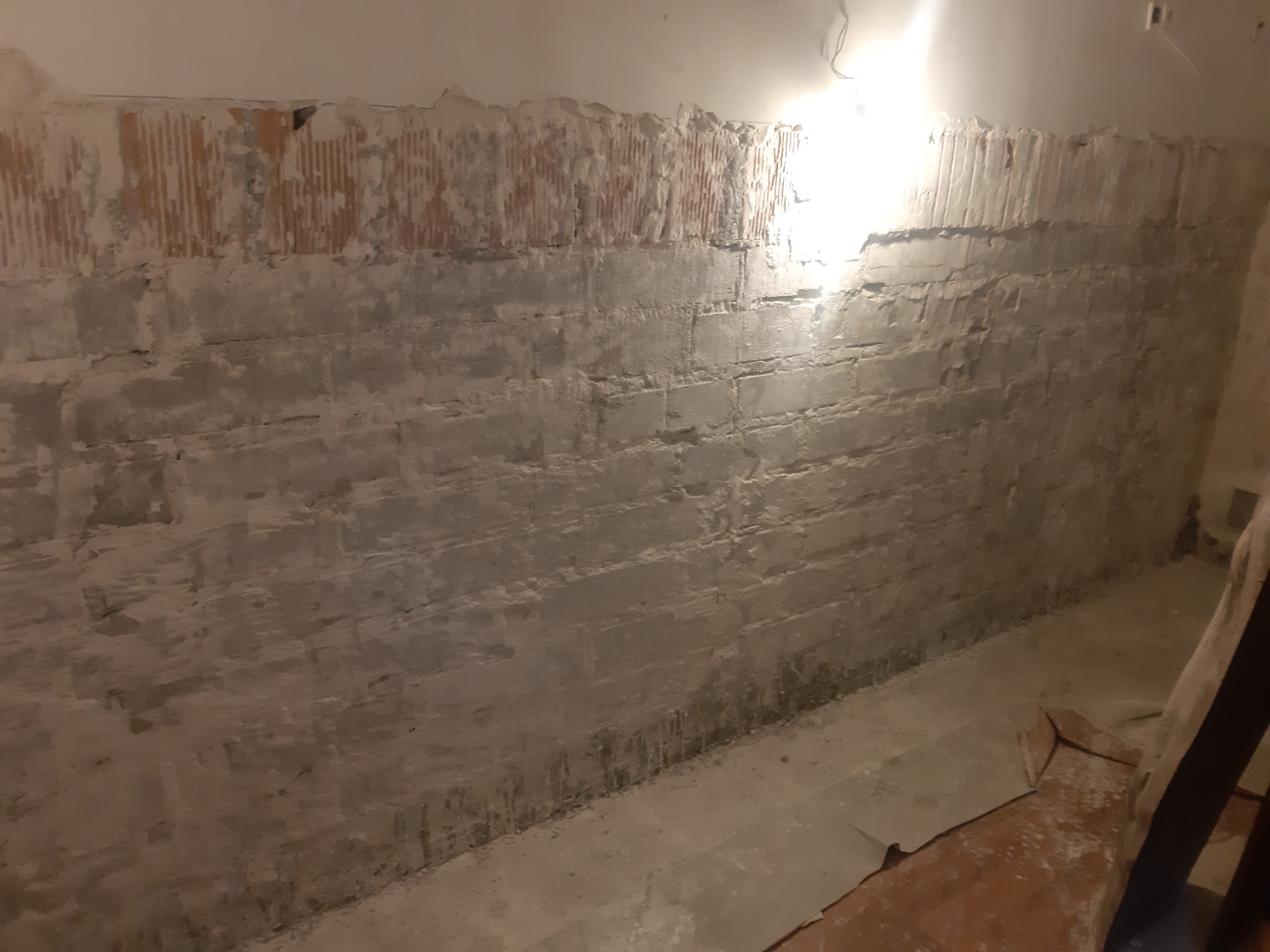 Ściana z usuniętym tynkiem, widoczne ślady zawilgocenia i cegły, przygotowana do osuszania.