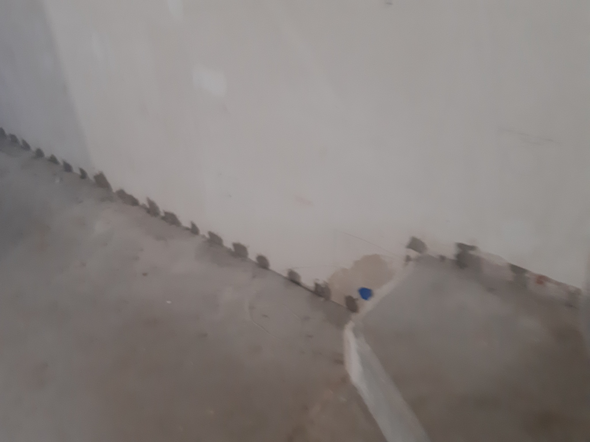 Przygotowanie do osuszania: Widok z dołu na wilgotną ścianę i podłogę z widocznymi śladami po usuniętych listwach przypodłogowych, na których widać pozostałości zaprawy.