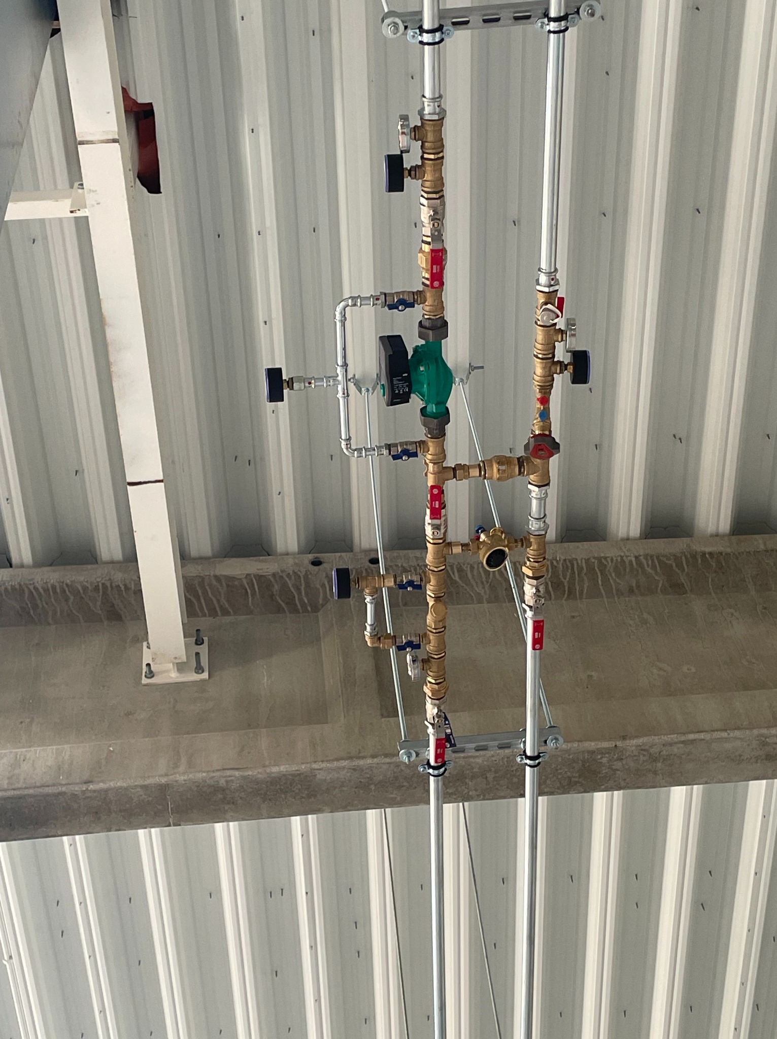 Węzeł centrali wentylacyjnej z nagrzewnicą CO w hali produkcyjnej. Rury miedziane i stalowe, zawory, pompa obiegowa. Montaż pod stropem z blachy trapezowej.