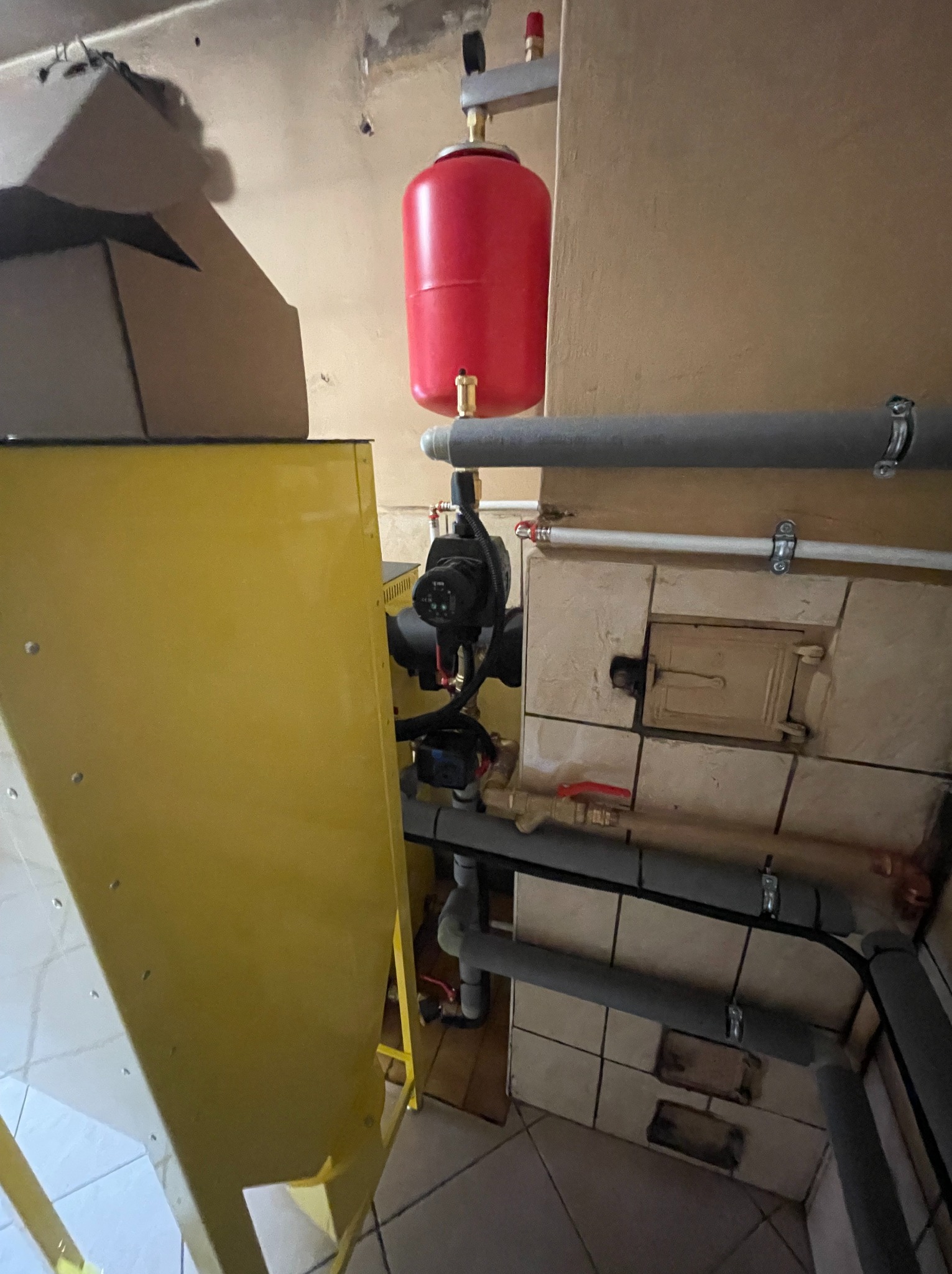 Węzeł centrali wentylacyjnej z nagrzewnicą CO w hali produkcyjnej. Widoczny czerwony zbiornik, żółta obudowa i szare rury. Ujęcie z dołu, podkreślające złożoność instalacji.