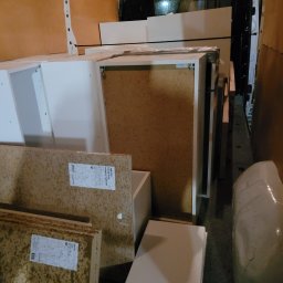 GWRD ANNA KACZMAREK - Wnętrze furgonetki załadowane elementami meblowymi, w tym płytami wiórowymi z etykietami i białymi szafkami, zabezpieczonymi do transportu.