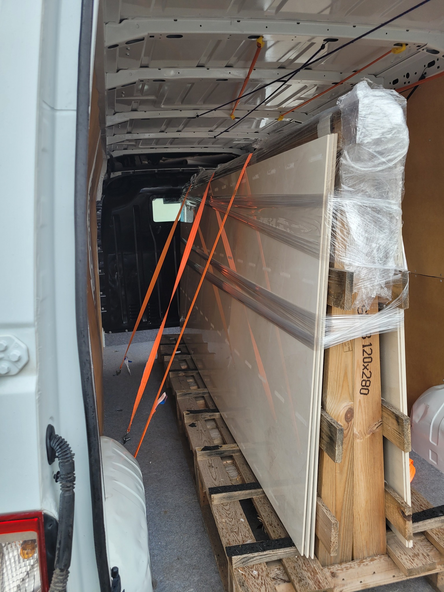 Transport płyt ceramicznych zabezpieczonych folią stretch i pasami w przestrzeni ładunkowej białego busa.