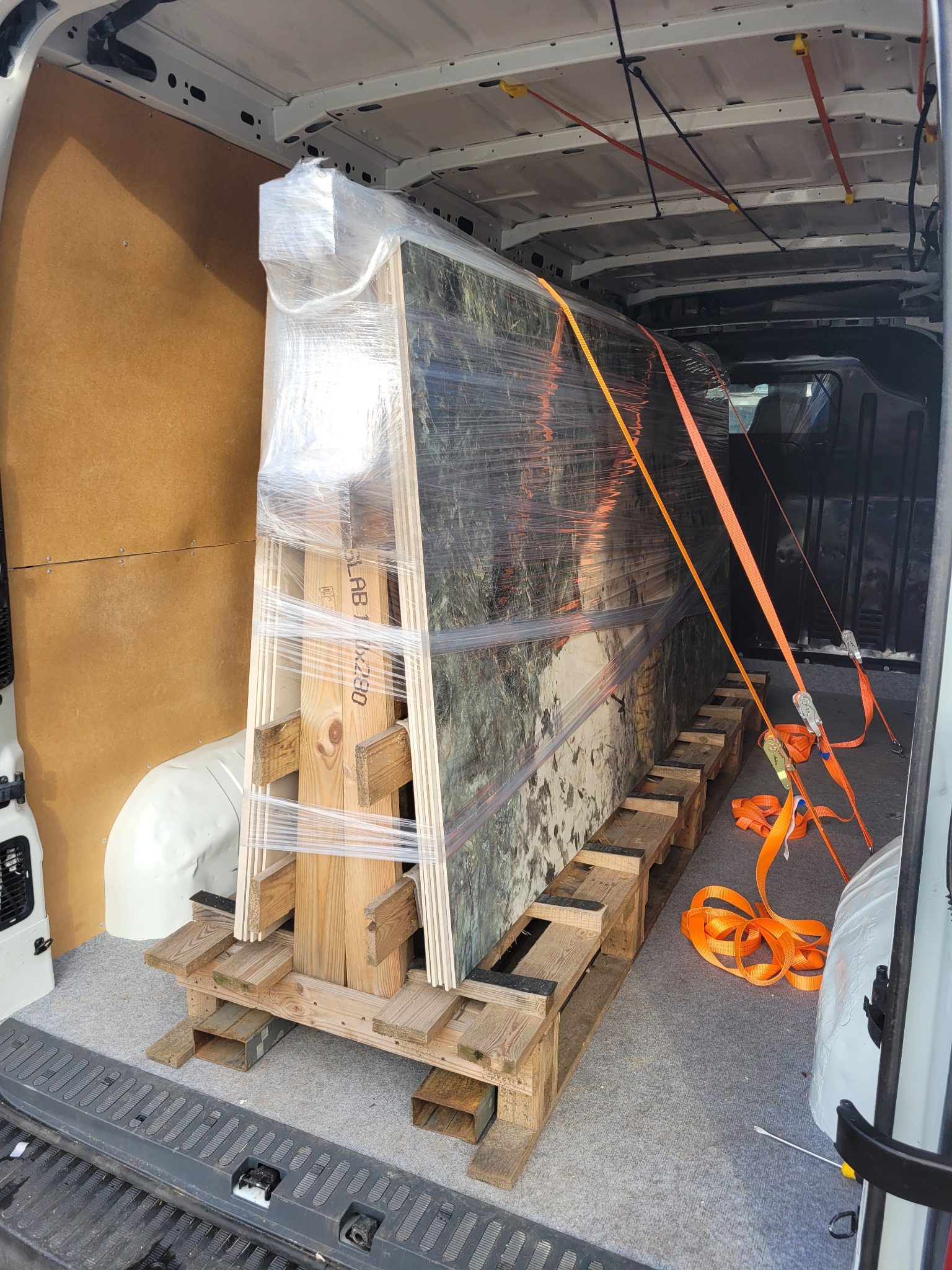 Obraz zabezpieczony folią stretch i pasami transportowymi wewnątrz furgonetki, umieszczony na drewnianej palecie.