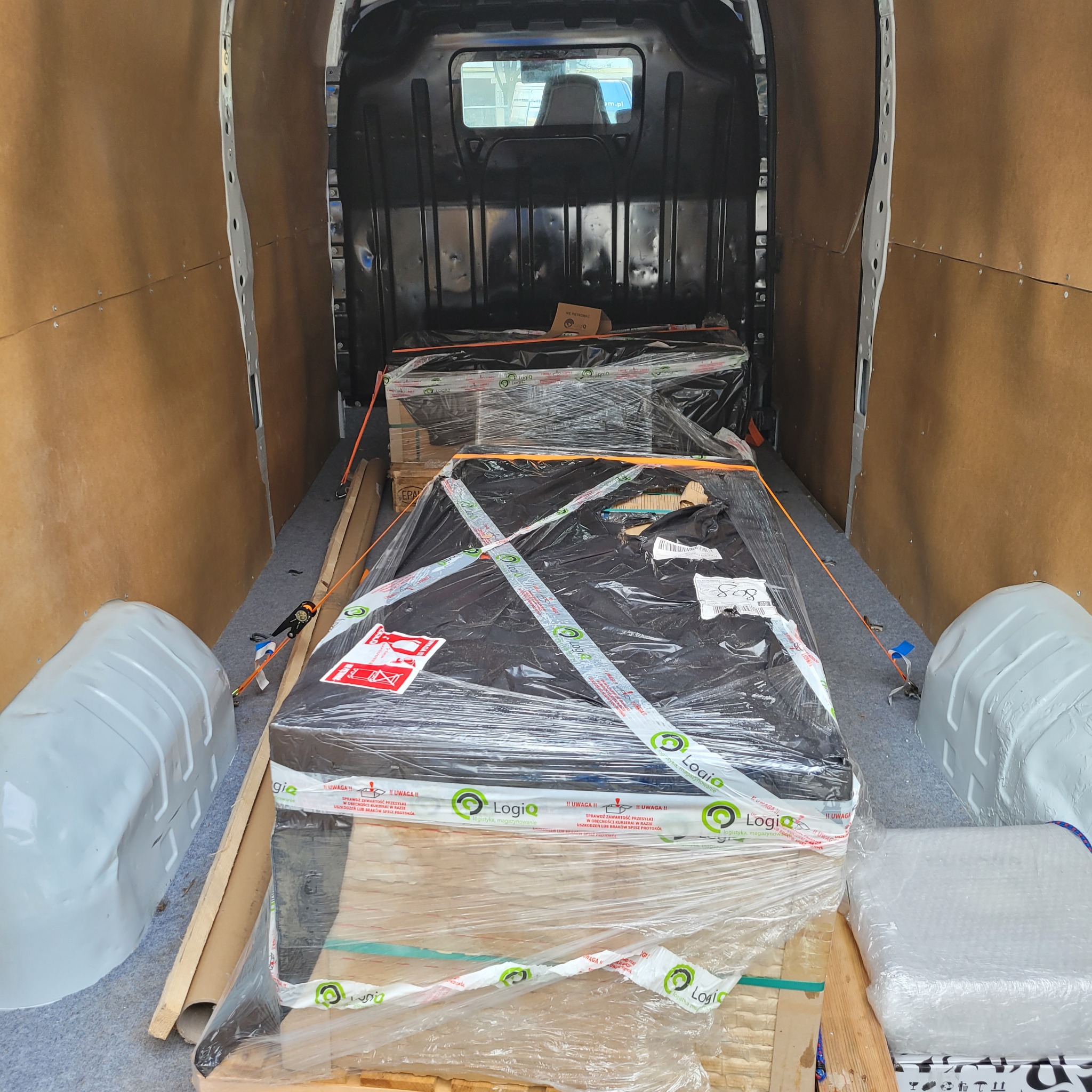 Wnętrze furgonetki z zabezpieczonym ładunkiem na paletach, owiniętym folią stretch i taśmą z logo 'Logiq', gotowym do transportu.