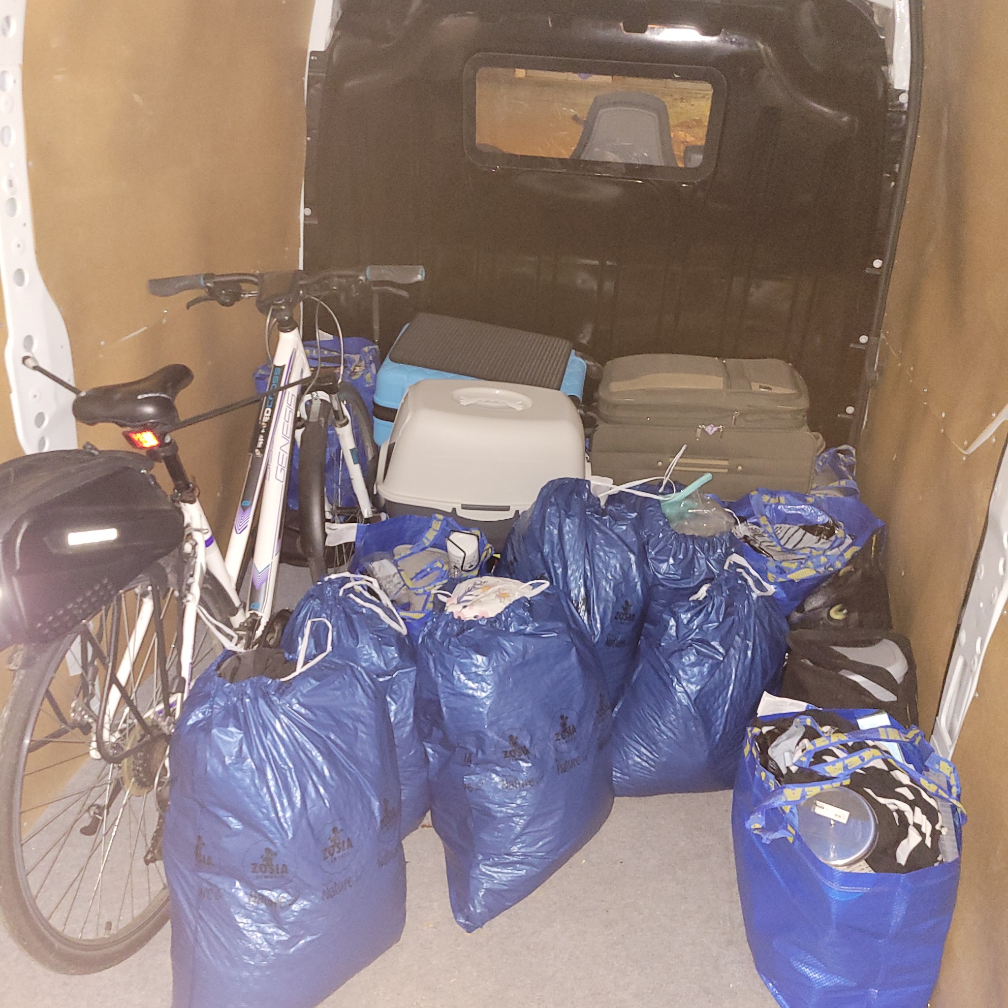 Wnętrze furgonetki załadowane workami z logo Zosia Nature, rowerem Genesis, kuwetą dla kota i walizkami, gotowe do transportu.