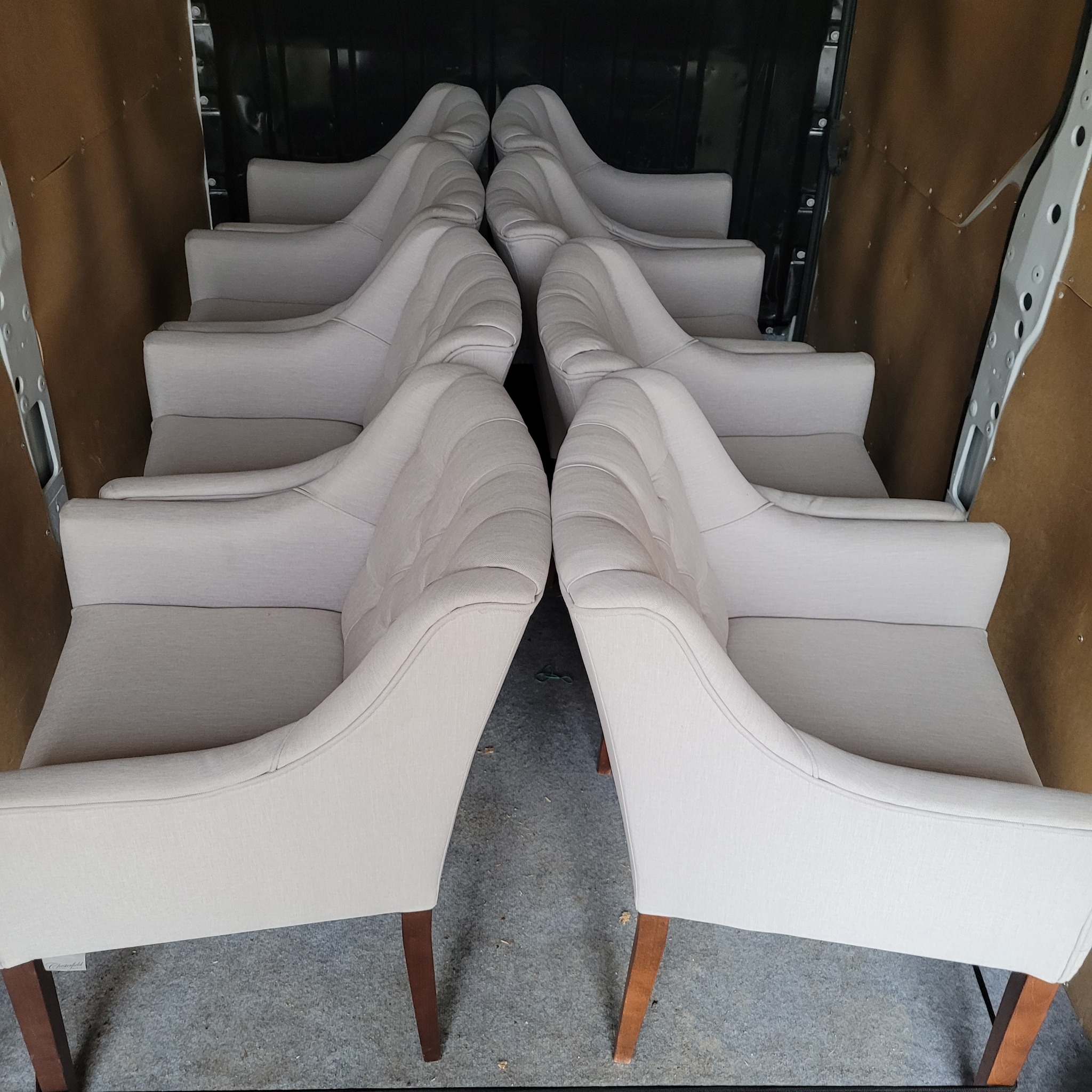 Rząd beżowych foteli z drewnianymi nogami, ustawionych ciasno wewnątrz przestrzeni ładunkowej samochodu dostawczego, gotowych do transportu.