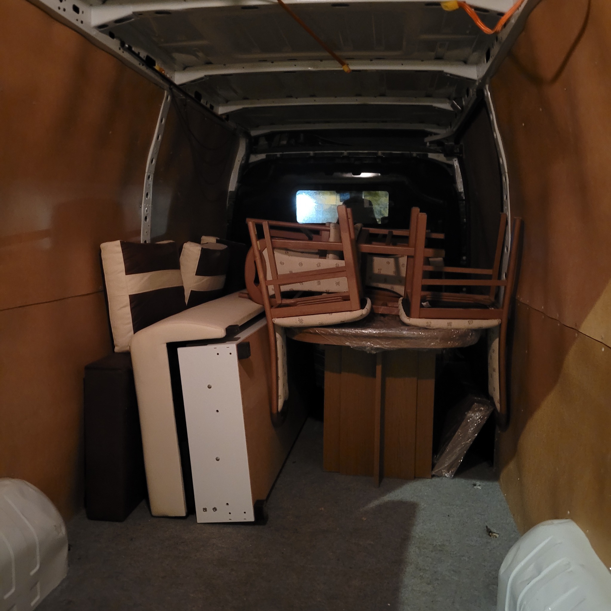 Wnętrze furgonetki załadowane meblami: rozłożony stół z krzesłami, sofa z poduszkami i szafka, przygotowane do transportu.