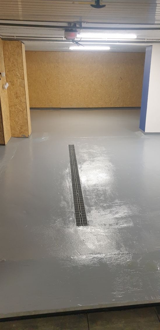 Szara, błyszcząca posadzka z odpływem liniowym w pomieszczeniu z płytami OSB na ścianach.