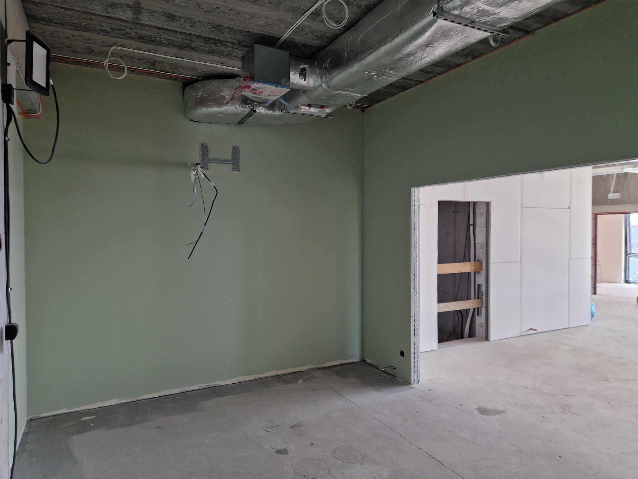 Wnętrze w trakcie prac wykończeniowych: pomalowane ściany na zielono, widoczne instalacje pod sufitem i surowe podłoże. W tle ścianki działowe z płyt gipsowych.