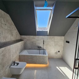 HYDBUD - Nowoczesna łazienka na poddaszu z czarnym sufitem, wykończona płytkami imitującymi kamień, z wanną podświetloną od dołu, bidetem i oknem dachowym, widoczne wystające kable.
